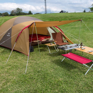Snow Peak tent set up on a grassy field with camping furniture and cooking gear