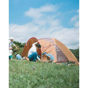 Family setting up a brown Snow Peak tent in a grassy field