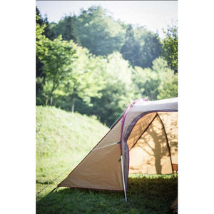 Tan and maroon camping tent set up on a grassy hill near a forest