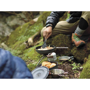 Person cooking food in a pan on a portable camping stove in a forest setting