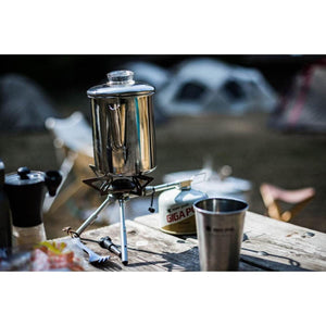 Snow Peak stainless steel coffee percolator on a camping stove with a fuel canister on a wooden table