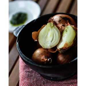 Whole and halved brown onions in a black bowl on a red and white checkered cloth
