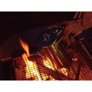 Snow Peak stainless steel kettle on a camping grill over an open fire