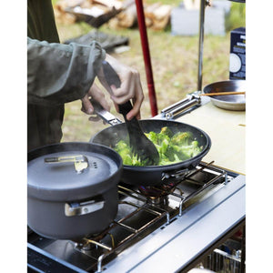 Person cooking broccoli in a frying pan on a portable camping stove
