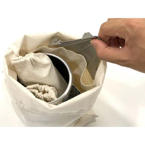 Hand placing a metal coffee dripper into a canvas drawstring storage bag