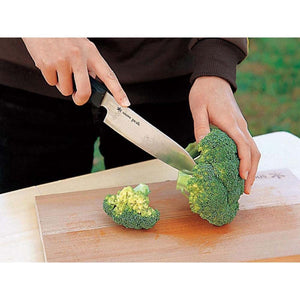 Person cutting broccoli on a wooden board with a Snow Peak knife
