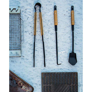 Black metal campfire tongs, poker, and spatula with wooden handles on snow