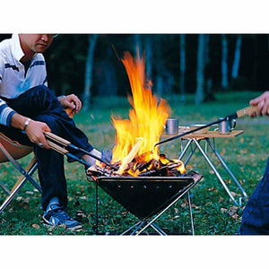 Person using metal tongs to adjust burning wood in a portable triangular fire pit outdoors