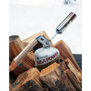 Snow Peak Giga Power torch attached to a fuel canister resting on a pile of firewood