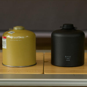 Snow Peak yellow gas canister next to a black Anker portable power bank on a wooden surface