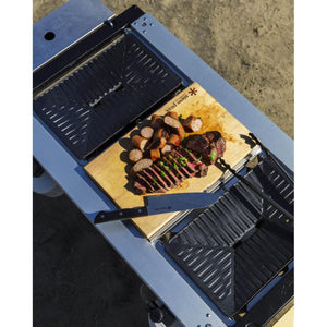 Snow Peak cutting board with sliced steak and sausages on a metal outdoor cooking table