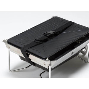 Snow Peak portable grill with black griddle plate secured by a black nylon strap