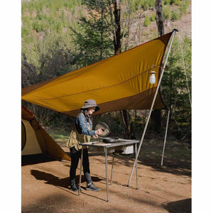 Person cooking at a Snow Peak outdoor kitchen table under a yellow tarp