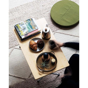 Snow Peak bamboo table with pastries, a kettle, magazines, and a decorative tray on a textured rug
