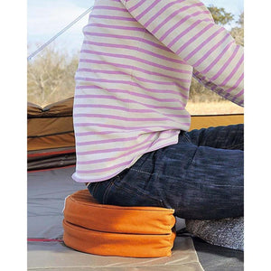 Person sitting on a round orange camping cushion inside a tent