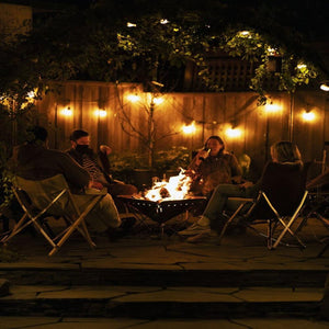 People sitting in Snow Peak folding chairs around a fire pit on a stone patio at night