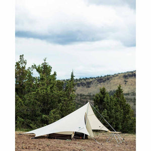 Snow Peak tent set up in a field with trees and hills in the background
