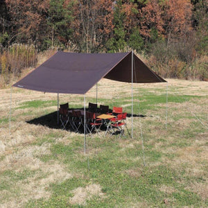 Snow Peak brown tarp set up over a folding table and chairs in a grassy field