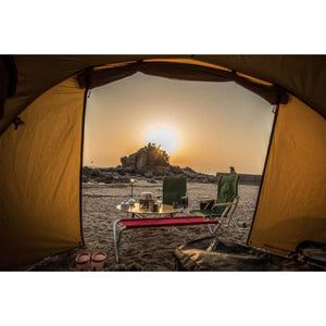 Snow Peak camping furniture set up on a beach at sunset viewed from inside a tent