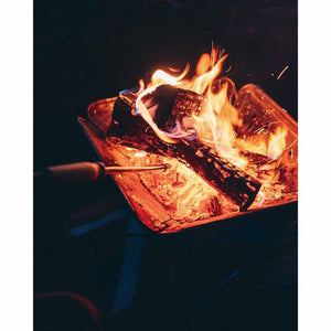 Snow Peak fire pit with burning logs and a metal fire poker