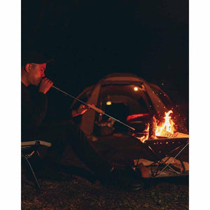 Person using a Snow Peak fire blower to stoke a campfire at night