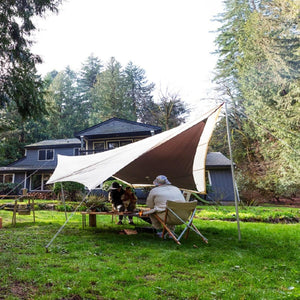 People sitting under a Snow Peak tarp in a backyard