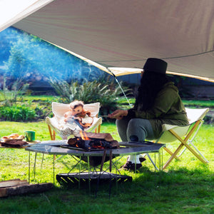Person and child sitting in Snow Peak chairs by a campfire under a tarp