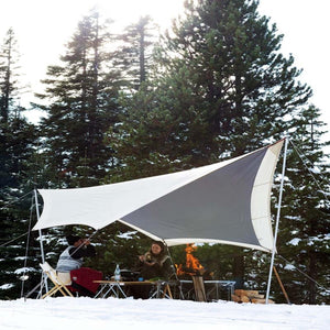 Snow Peak tarp set up over a table and chairs in a snowy forest with a campfire