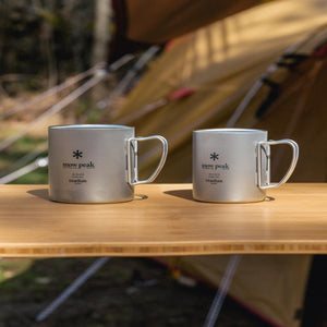 Two Snow Peak titanium double wall mugs on a wooden table with a tent in the background
