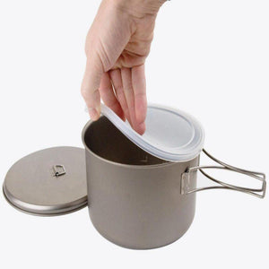 Hand placing a silicone lid onto a titanium camping pot with folding handles
