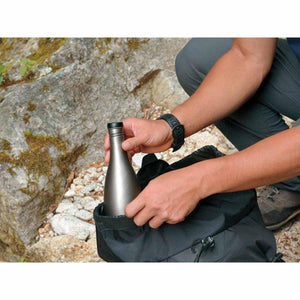 Person placing a metallic water bottle into a black backpack outdoors