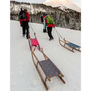 People pulling Snowline wooden sleds with woven seats up a snowy mountain slope