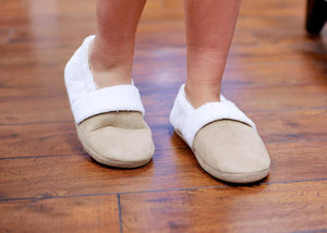 Child wearing tan suede slippers with white faux fur trim on a wooden floor