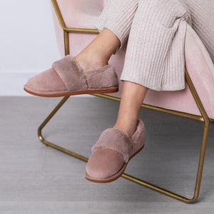Person wearing mauve faux fur lined suede slippers while sitting in a pink velvet chair