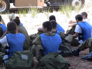 Group of people wearing TechKewl blue cooling vests sitting on the ground