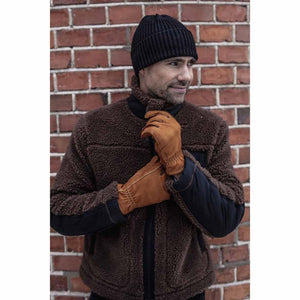 Man wearing Hestra tan leather gloves and a brown fleece jacket against a brick wall