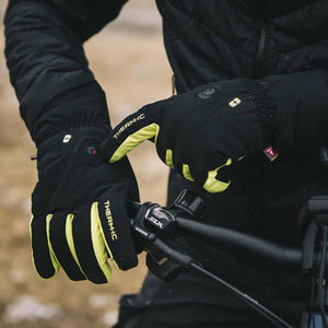 Person wearing black and yellow Therm-ic heated cycling gloves while holding handlebars