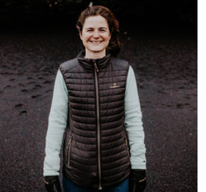 Woman wearing a black Therm-ic quilted vest over a light blue long sleeve shirt