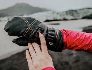 Hand pressing the power button on a black Therm-ic heated mitten