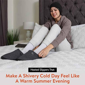 Person wearing grey heated slippers while sitting on a bed