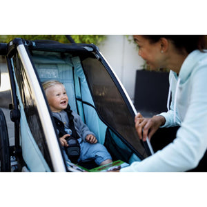 Child sitting in a Thule bike trailer while an adult interacts with them