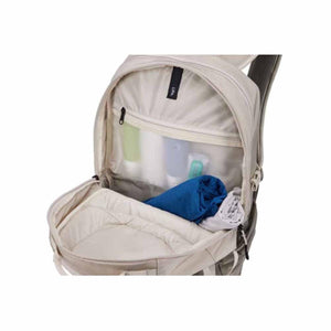 Open interior of a beige Thule backpack showing a zippered mesh pocket and folded clothing