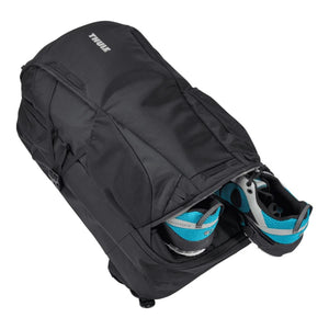 Thule black backpack with a zippered bottom compartment containing a pair of blue and grey running shoes