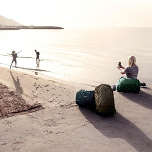 Thule backpacks and duffel bags on a beach with people in the background