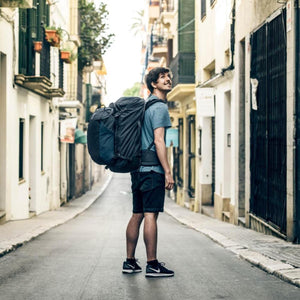 Person wearing a black Thule travel backpack while walking down a narrow city street