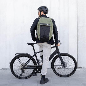 Person wearing a green Thule backpack and a bicycle helmet standing with a black bicycle