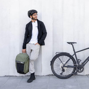 Person in cycling gear holding a green Thule backpack next to a bicycle