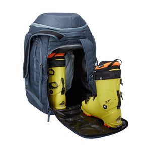 Blue Thule ski boot backpack with one yellow ski boot inside and one yellow ski boot placed on the open front flap