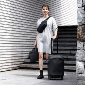Person wearing a Thule crossbody bag while carrying a laptop bag and rolling a Thule suitcase