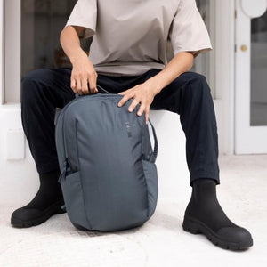 Person sitting while holding a grey Thule backpack
